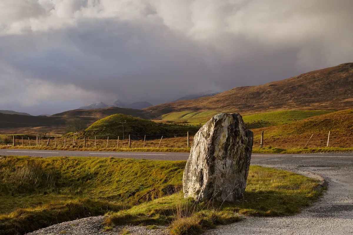 A standing stone beside a winding road under heavy clouds