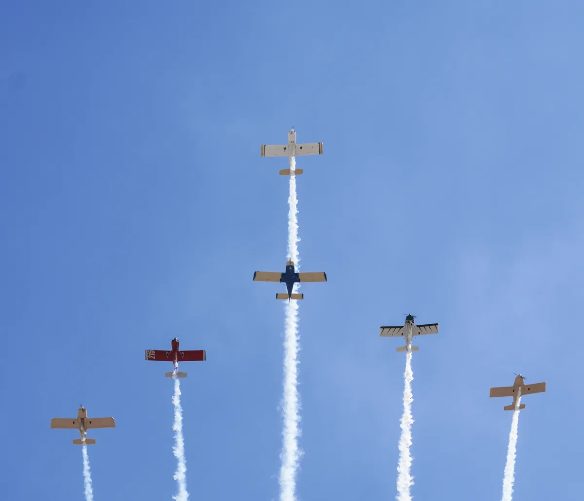 Five propeller aircraft climbing in formation with white smoke trails
