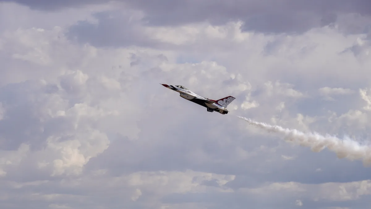 A fighter jet trailing white smoke across a cloudy sky