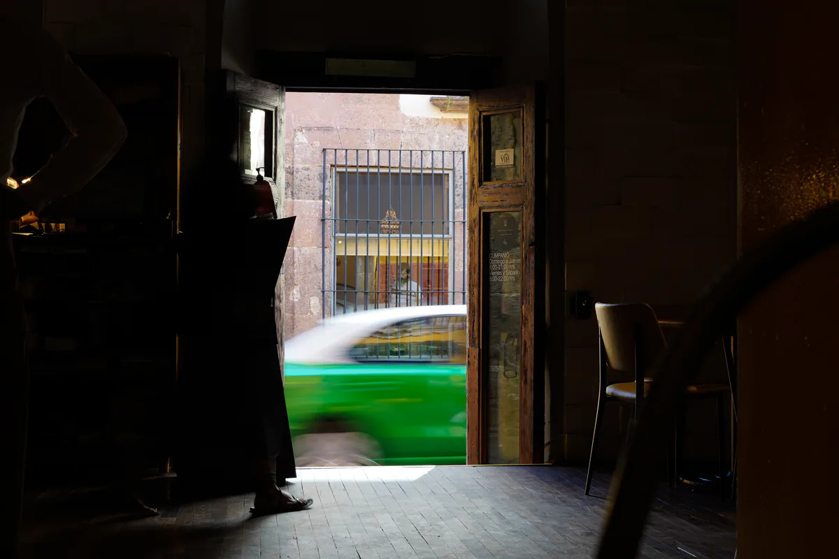 A dark interior looking out through a doorway as a green car passes