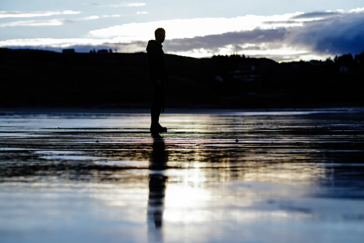 A figure in silhouette on wet sand that mirrors the sky